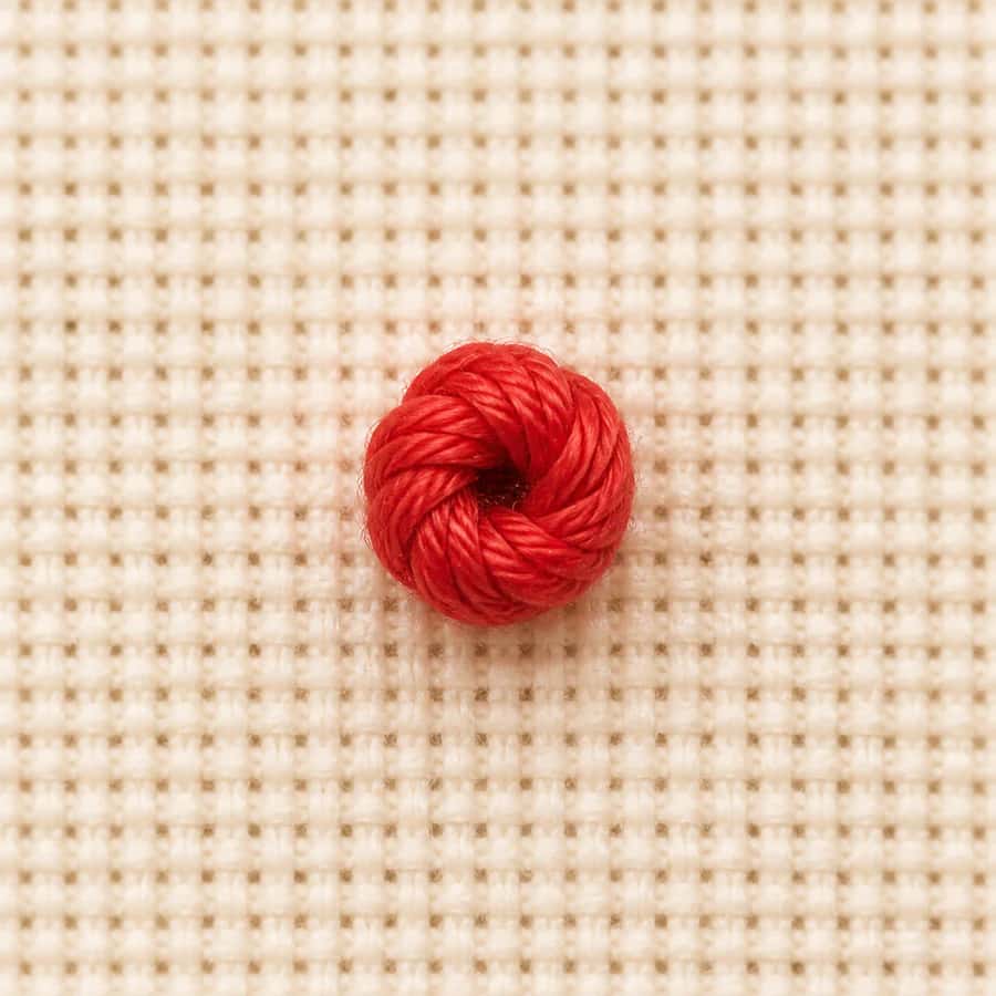 Macro view of a raised coral French knot on cream Aida cloth
